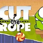 Një qenush jeshil me sy të mëdhenj dhe dhëmbë të bardhë, ulur pranë një karameleje të varur pranë tekstit të madh me fjalët Cut the Rope