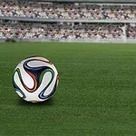 Top i bardhë me dizajne shumëngjyrëshe mbi një fushë gjelbër futbolli me tribuna të mbushura me spektatorë