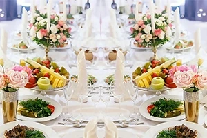 Tavolinë festive e shtruar me pjatanca, fruta të freskëta, lule dhe dekorime elegante